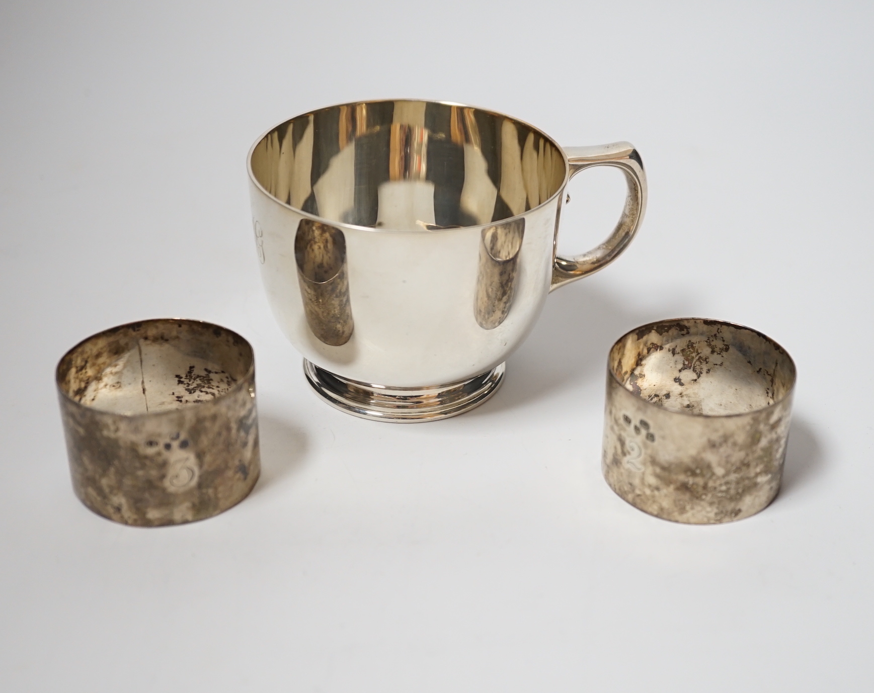 A George V silver cup, with single handle, Searle & Co, London, 1932, height 61mm, together with a pair of late Victorian silver napkin rings, Charles Edwards, London, 1899, 8oz.